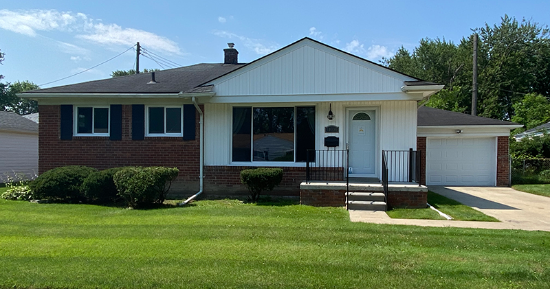 A white brick house with green grass in front of it.