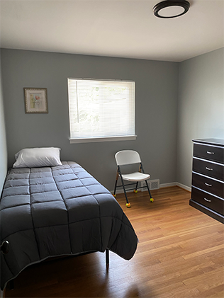 A bedroom with a bed, chair and dresser.