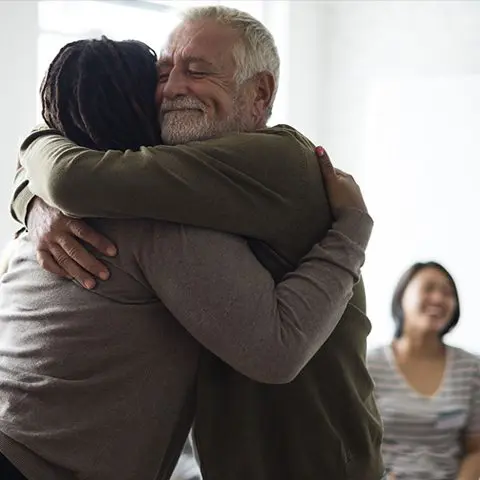 A man and woman hug in front of another person.