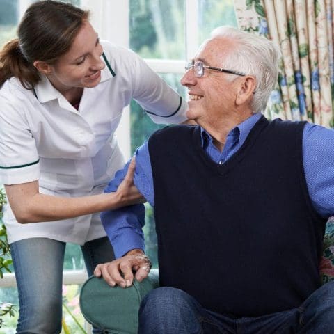 A woman is helping an older man sit on the couch.