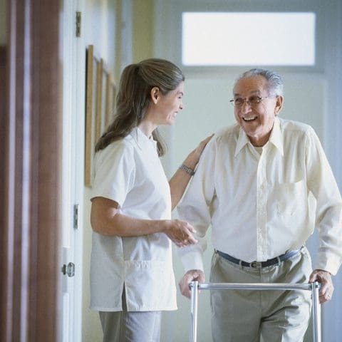 A woman helping an old man walk with a walker.